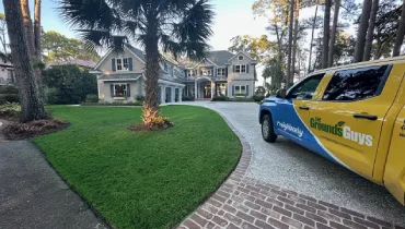A uniformly green painted lawn near a branded The Grounds Guys truck.