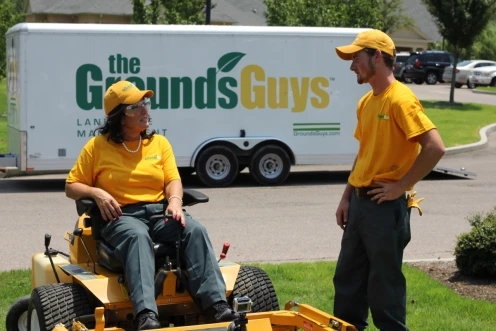 Two Grounds Guys service professional talking, with a branded company trailer behind them.
